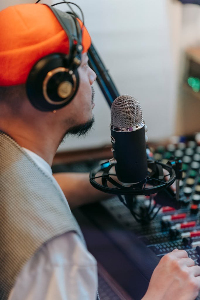 Man wearing headphones and knitted cap recording audio at a studio microphone.