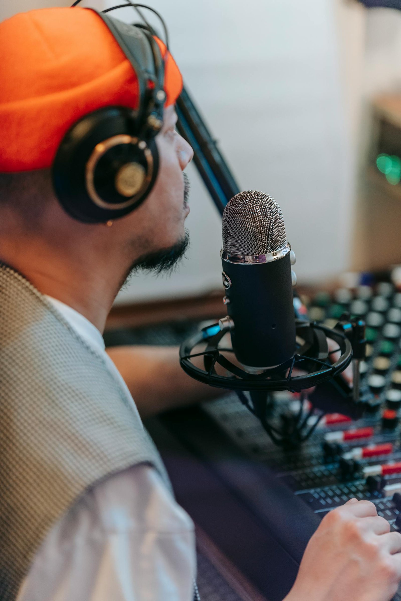 Man wearing headphones and knitted cap recording audio at a studio microphone.