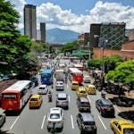 Street scene in Medellín, Colombia, showcasing bustling traffic, taxis, and towering buildings on a sunny day.