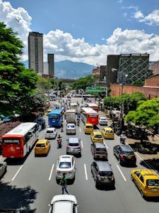 Street scene in Medellín, Colombia, showcasing bustling traffic, taxis, and towering buildings on a sunny day.