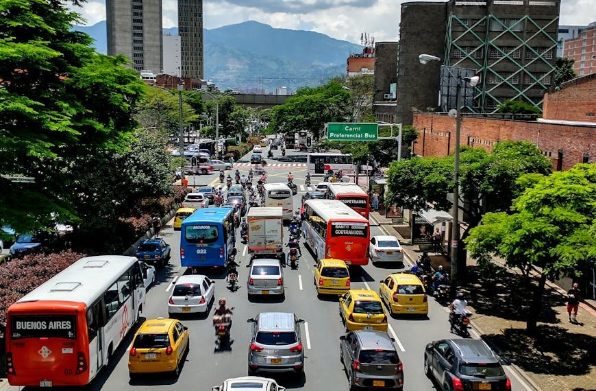 Street scene in Medellín, Colombia, showcasing bustling traffic, taxis, and towering buildings on a sunny day.